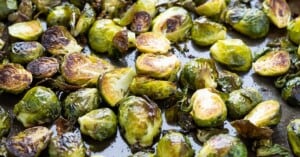 Side view of a pan of roasted brussel sprouts showing crisp browned leaves and flecks of salt and red pepper flakes.