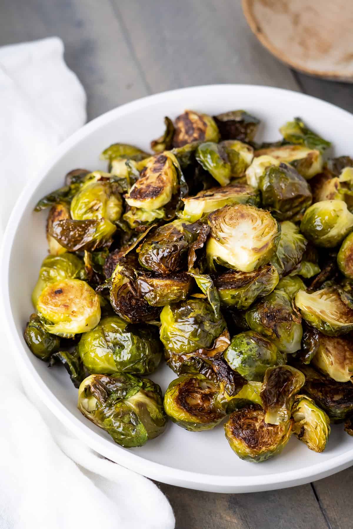Side view of a large pile of crispy roasted brussel sprouts in a bowl with browning edges and sea salt.