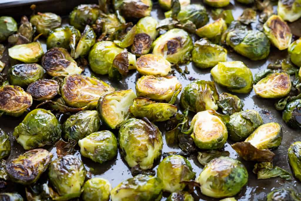Side view of a pan of roasted brussel sprouts showing crisp browned leaves and flecks of salt and red pepper flakes.