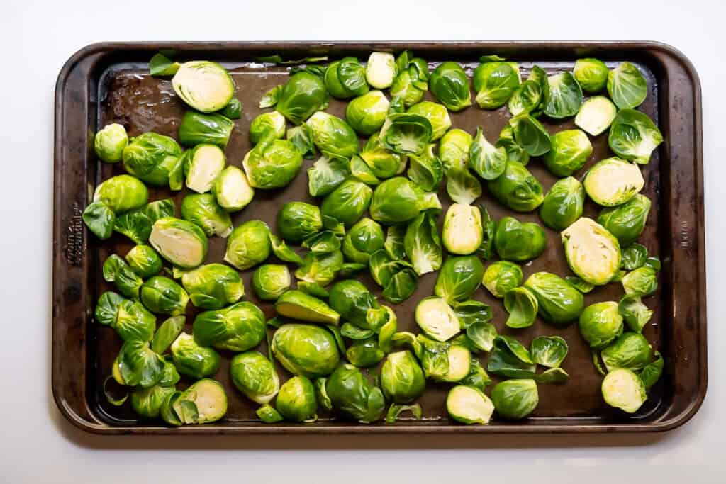 Overhead view of a metal baking sheet with uncooked brussel sprout halves tossed in oil.