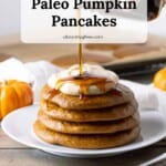 Four fluffy paleo pumpkin pancakes topped with a swirl of pumpkin whipped cream and a drizzle of maple syrup.