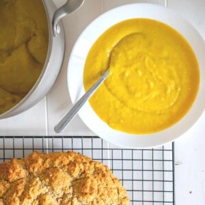 Overhead view of a bright golden bowl of pureed beet soup beside a fresh loaf of gluten-free Irish Soda Bread.