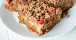 An up close view of the corner of a piece of gluten free rhubarb cake to show the layers and crisp topping.