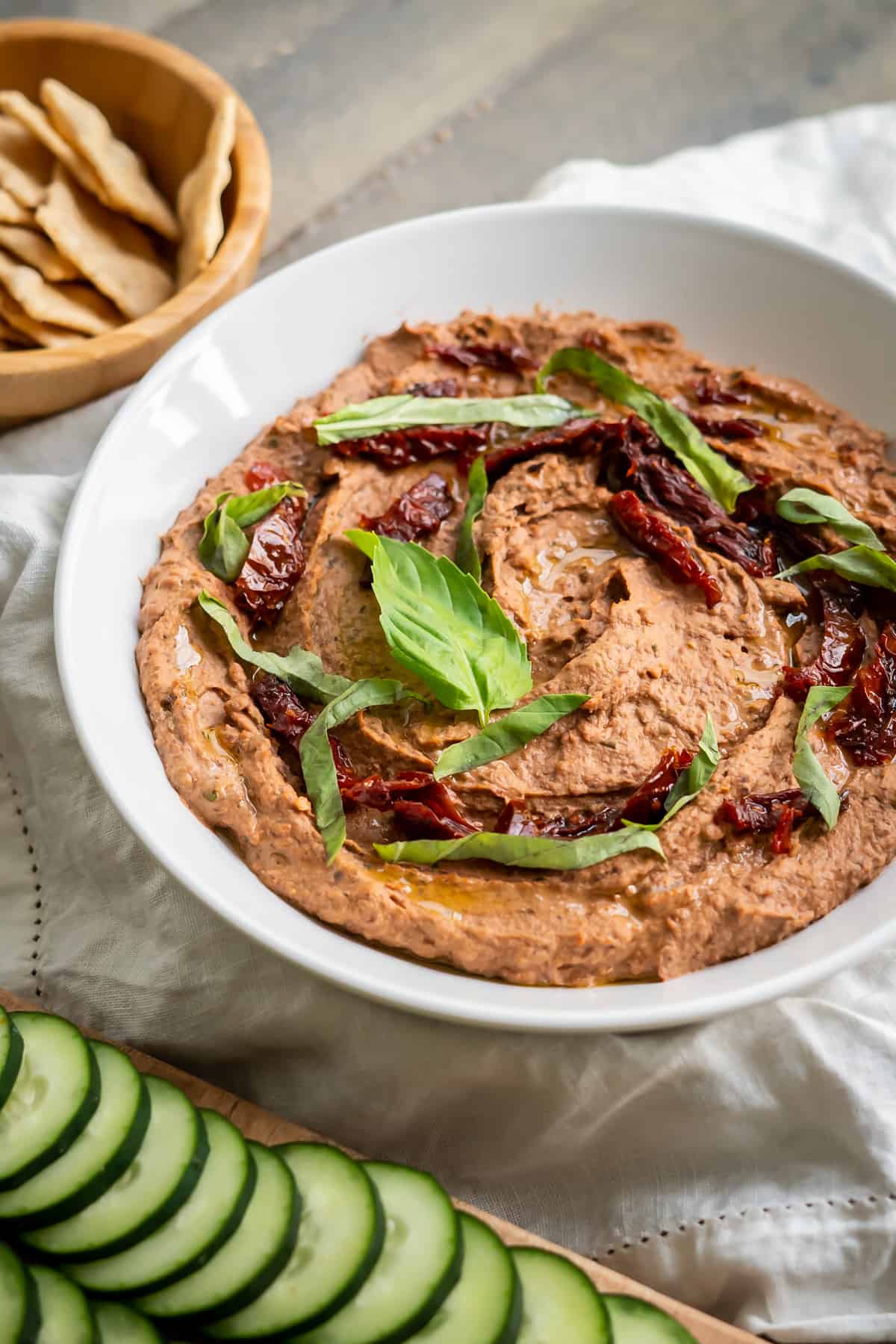 A bowl of creamy black bean hummus decorated with pieces of sun-dried tomatoes and basil leaves.