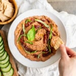 A serving bowl of black bean hummus with sun-dried tomatoes and basil.