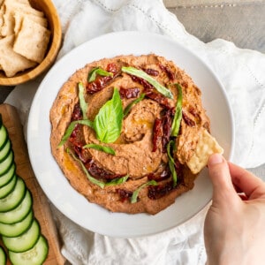 A serving bowl of black bean hummus with sun-dried tomatoes and basil.