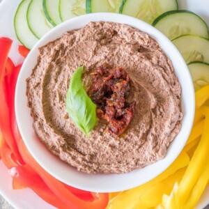 Black bean hummus topped with a basil leaf and sun-dried tomatoes to garnish and served with fresh cut vegetables.