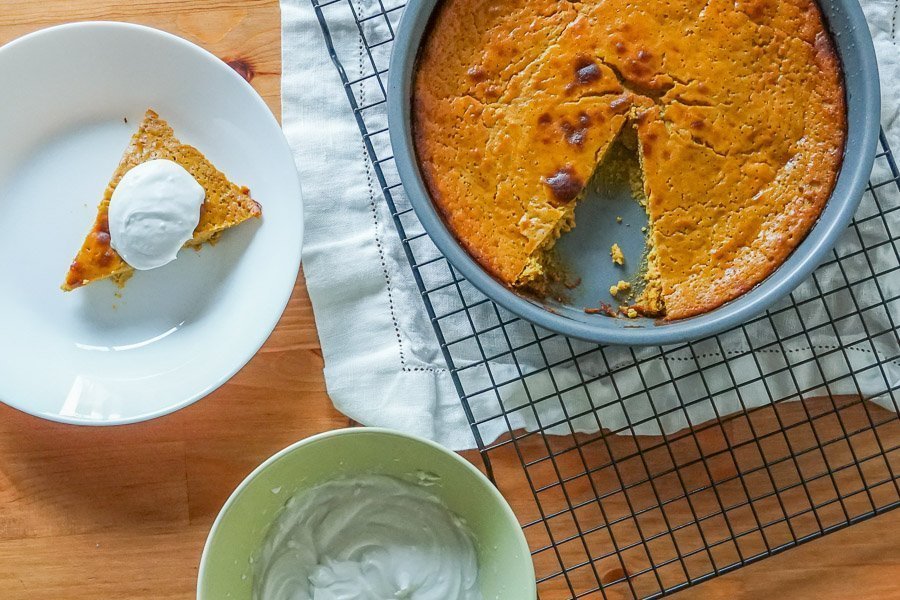 Gluten free pumpkin pie in pie dish with a slice remove onto a round plate topped with cream.