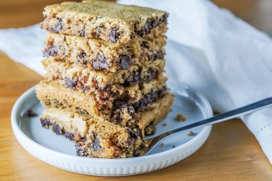 A stack of paleo and gluten-free blondies on a plate with a bite removed from one to show the soft and chewy texture!
