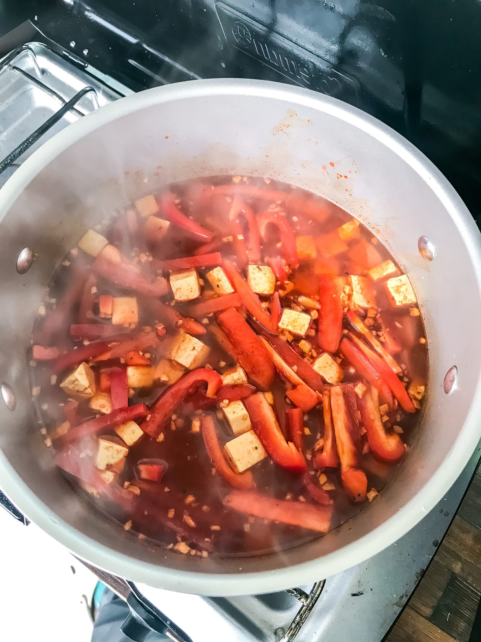 Soup simmering with tofu, ginger, garlic, red bell pepper, red curry paste, and broth.