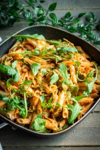 Sun-dried tomato pasta sauce, pasta, and arugula mixed together in a pan