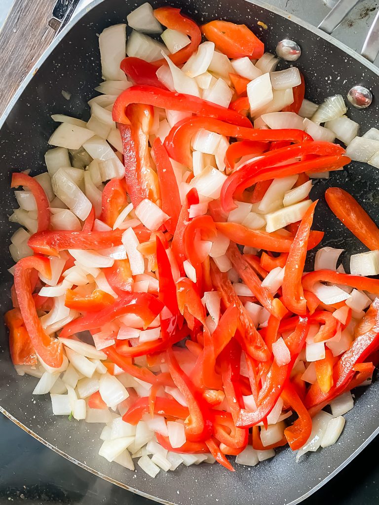 Overhead view of onion and bell pepper cooking in a frying pan.