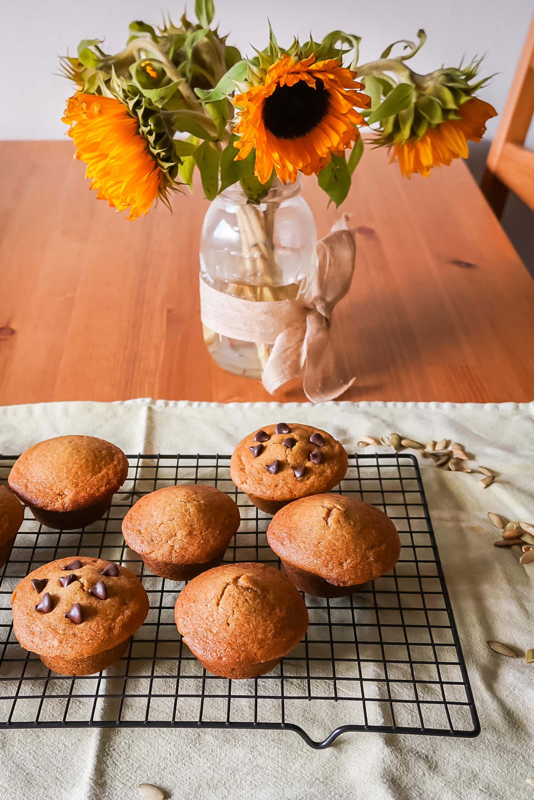 Side view of a cooling rack of gluten-free pumpkin muffins sitting beside a vase of fresh sunflowers.