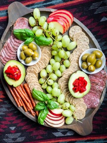 A gluten and dairy free charcuterie board with grapes, crackers, meats, and other nibbles.