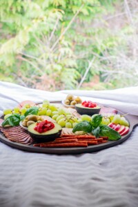 A gluten and dairy free charcuterie board set on a bed with a view of foliage outside.