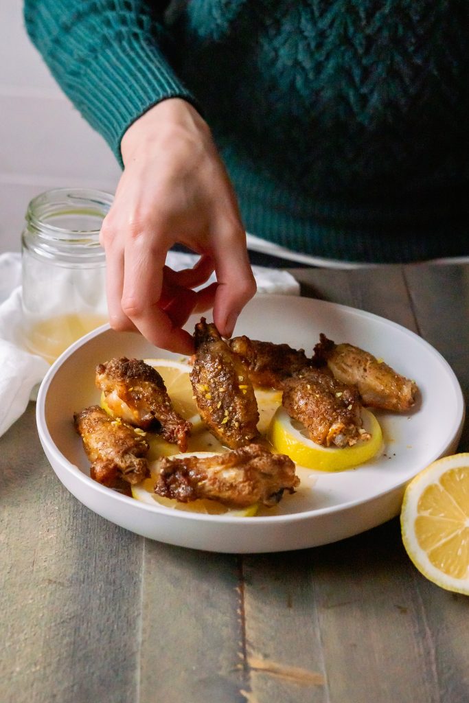 A hand picking up a lemon pepper wing from the serving plate.