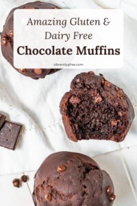 Three gluten free chocolate muffins arranged on a napkin. One with a bite missing to show the moist texture.