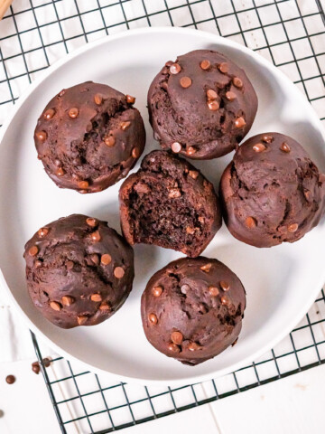 Top view of six gluten free chocolate muffins in a dish with a bite out of one to show the texture.