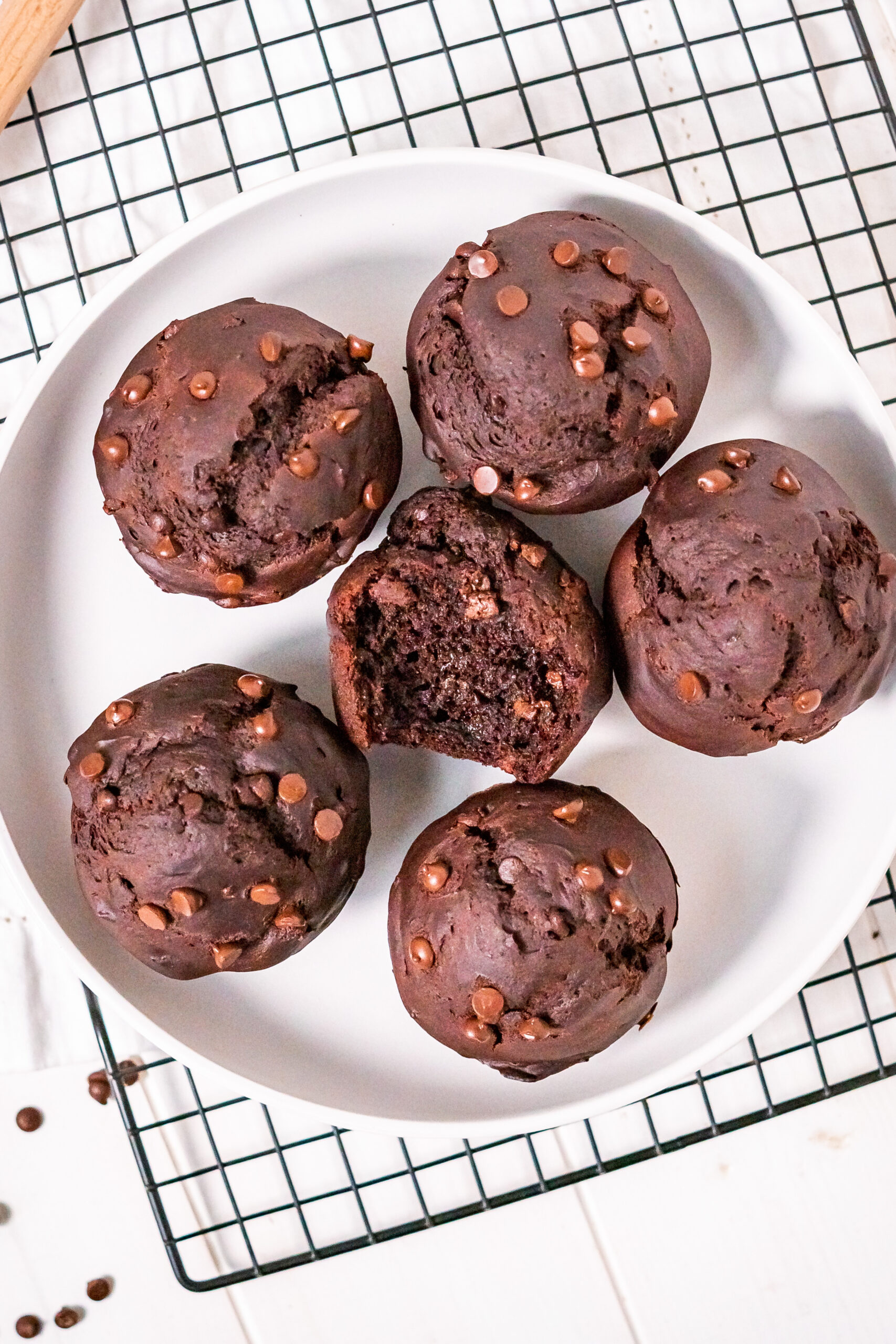 Top view of six gluten free chocolate muffins in a dish with a bite out of one to show the texture.