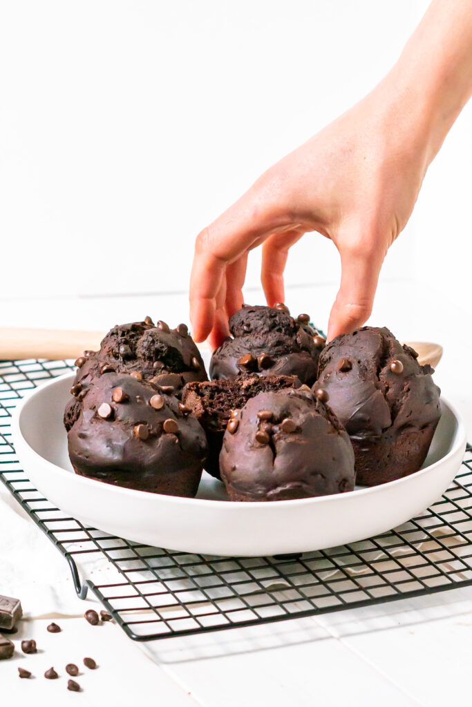 Side view of a hand reaching out to take one of the gluten free chocolate muffins from a plate of six.
