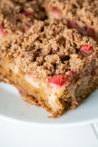 A zoomed in view of the corner of a piece of gluten free rhubarb cake to show the layers and crisp topping.