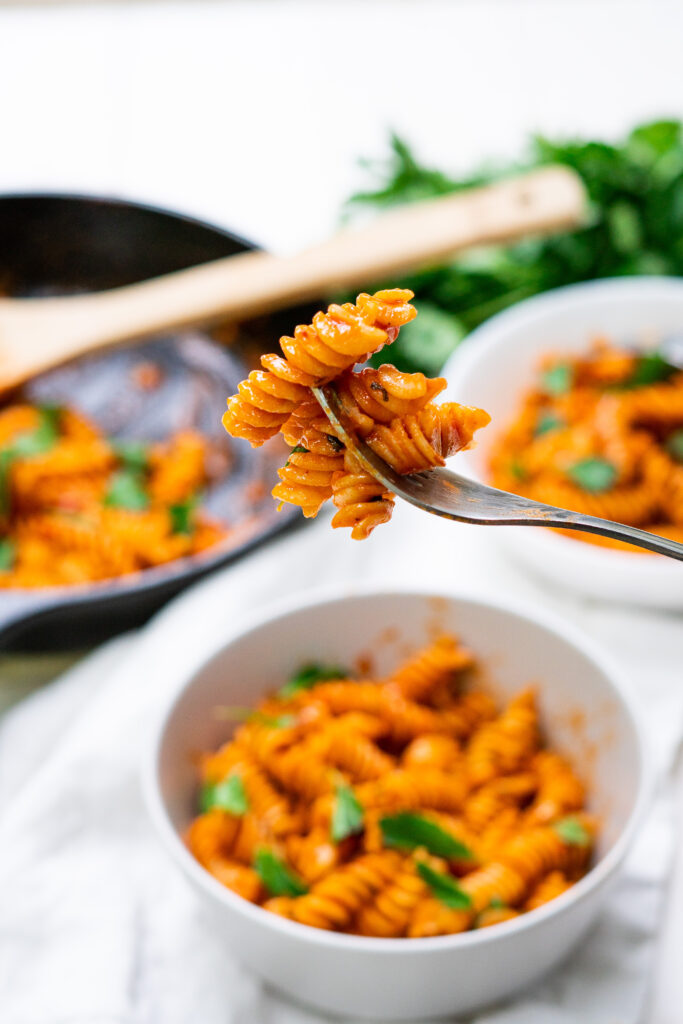 A bite of vegan vodka pasta on a fork hovering above a bowl of pasta.