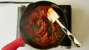Spatula stirring tomato paste in the skillet to make vodka sauce.