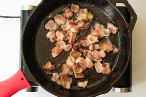 Overhead view of bacon pieces frying in a skillet.