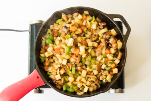 Overhead view of vegetables and potatoes fried with spices in a cast iron skillet.