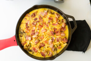 Southwest breakfast skillet ready for baking with vegetables, cheese, egg, and bacon layered in the skillet.