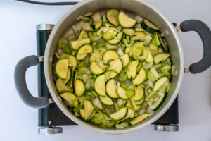 Overhead view of zucchini, onion, and celery cooking in a pot on a burner.