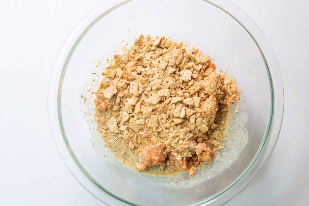 Baked salmon cake mixture layered in a bowl. From bottom: wet ingredients whisked together, salmon, crushed crackers.