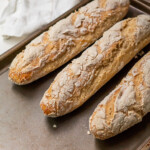 Three crusty gluten free french baguettes freshly baked on a pan.