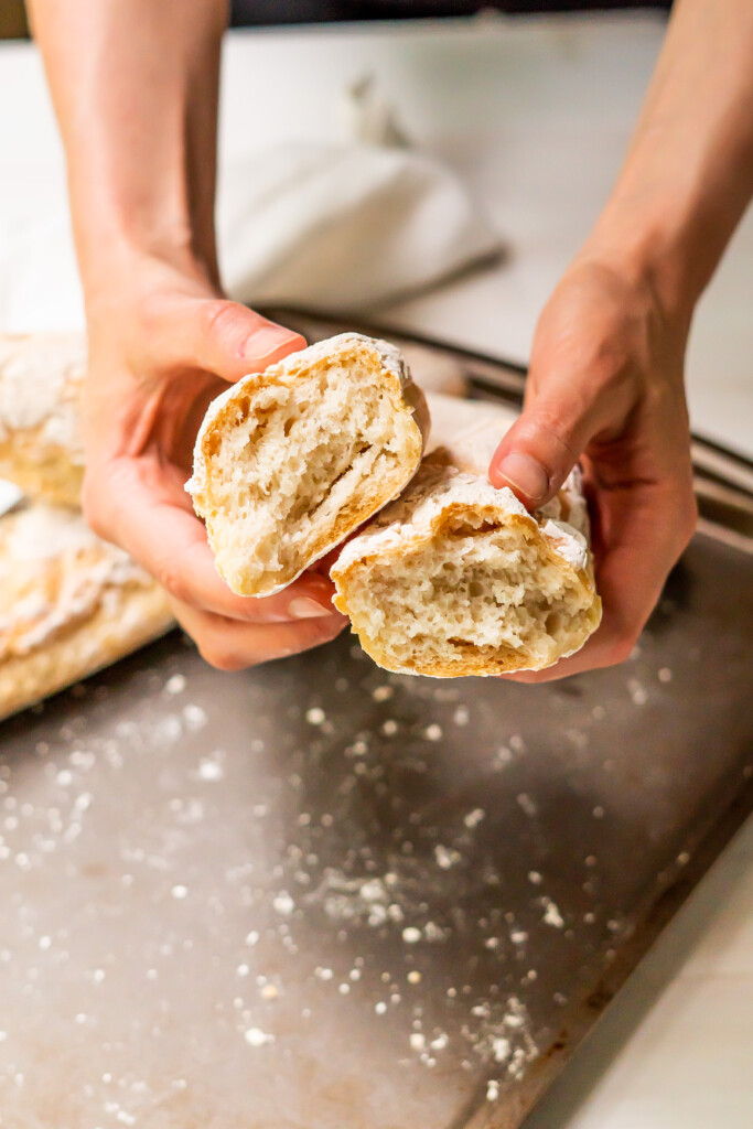 Hands holding a gluten free french baguette split in two to show the soft inside and crusty outside!