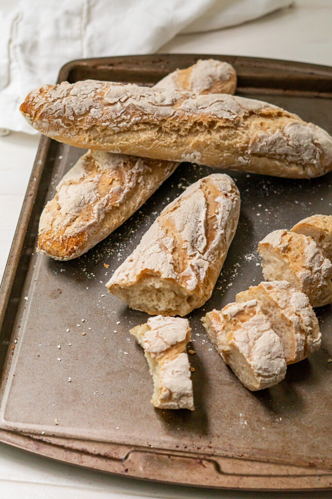 Two full gluten free french baguettes with a third sliced into pieces to show the crusty outside and soft inside.
