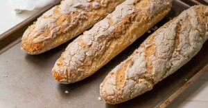 Three crusty gluten free french baguettes, freshly baked and on a baking sheet.