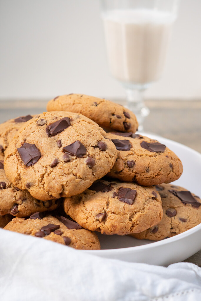 Side view of a plate of large soft almond flour chocolate chip cookies with a glass of dairy-free milk.