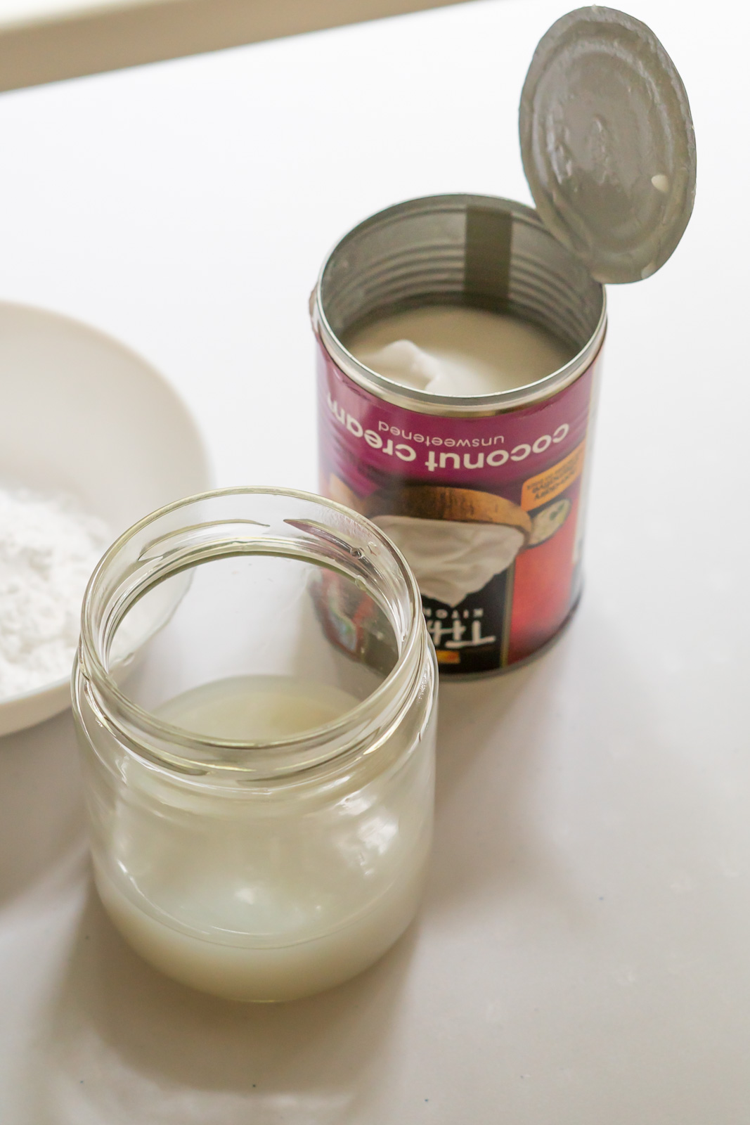 A can of coconut cream opened at the bottom with the liquid poured off into a separate jar.