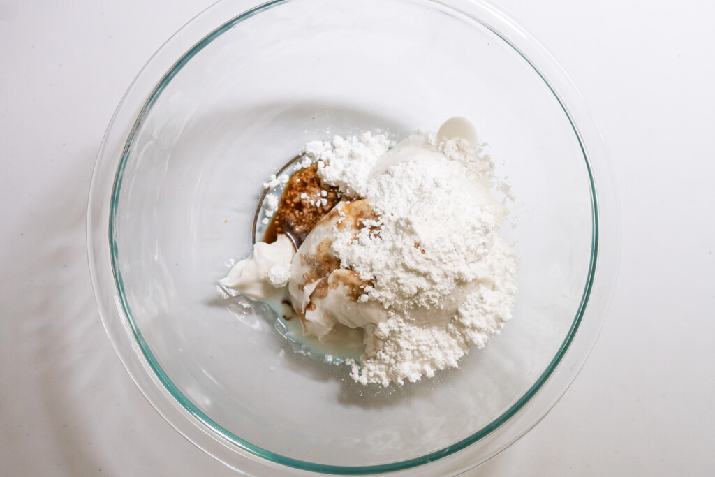 Overhead view of a large mixing bowl with coconut cream, confectioner's sugar, vanilla extract, and salt.