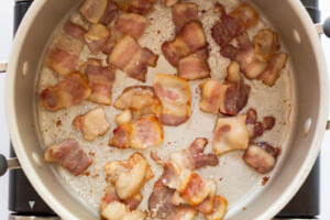 Overhead view of 1-inch pieces of bacon frying in a 5 quart dutch oven.
