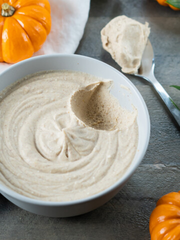 Side view of a bowl of vegan pumpkin spice whipped cream with a spoonful removed to show the soft and fluffy texture.