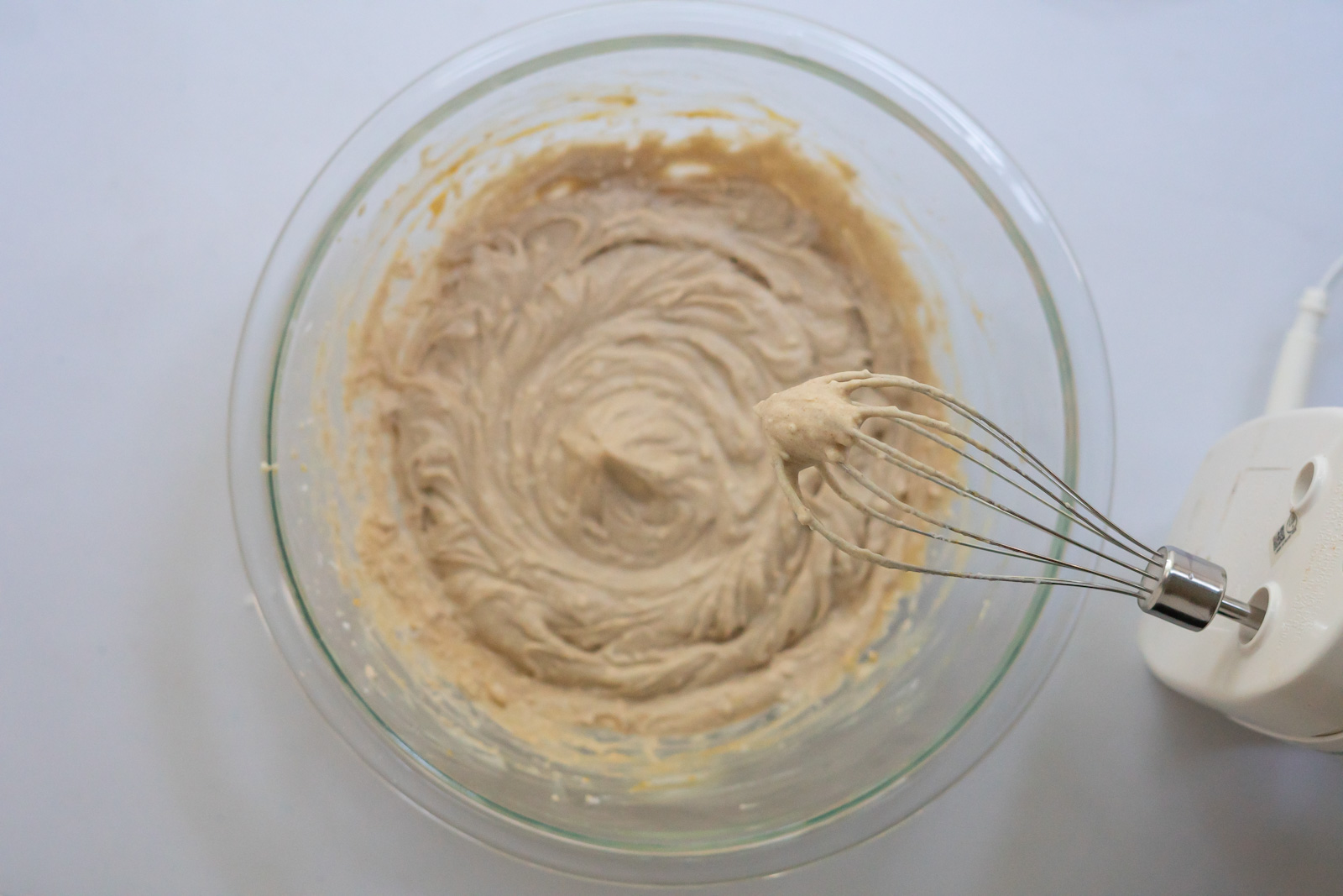 Overhead view of the well-mixed pumpkin whipped cream in a mixing bowl with electric mixer and whisk attachment.