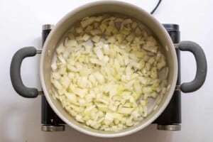 Overhead view of chopped onions cooking in a dutch oven with oil.