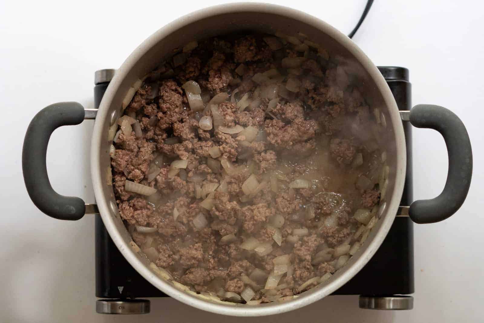 Overhead view of ground beef browning in a dutch oven with chopped onion.