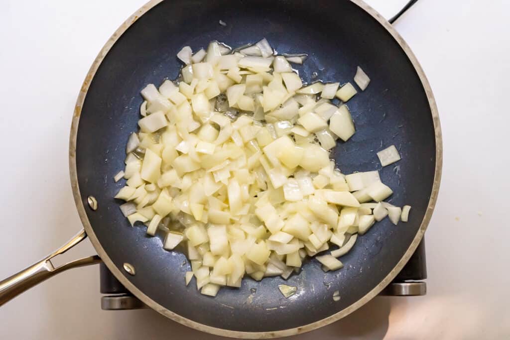 Overhead view of diced onions cooking in a skillet.