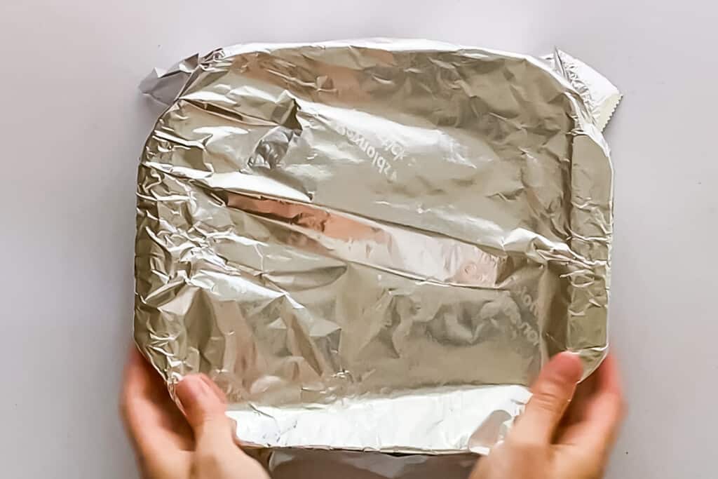 Overhead view of an 8 inch square dish covered with foil, and ready for baking.