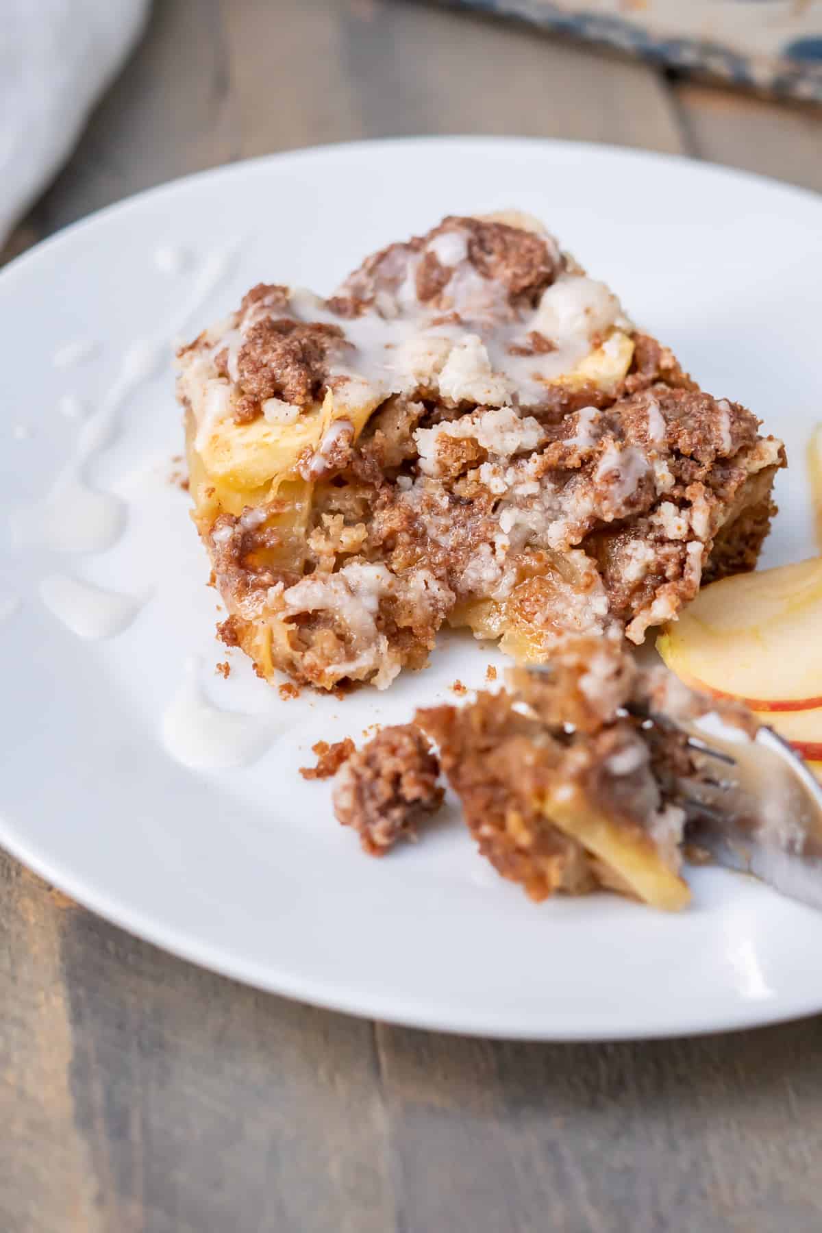 Side view of a square piece of gluten free apple coffee cake with a bite removed to show the soft cake, apple, and crumble layers.