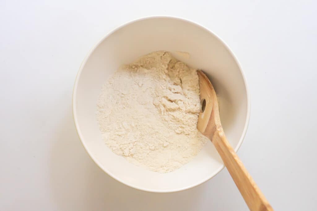 Overhead view of a bowl of dry ingredients fully mixed with a wooden spoon.