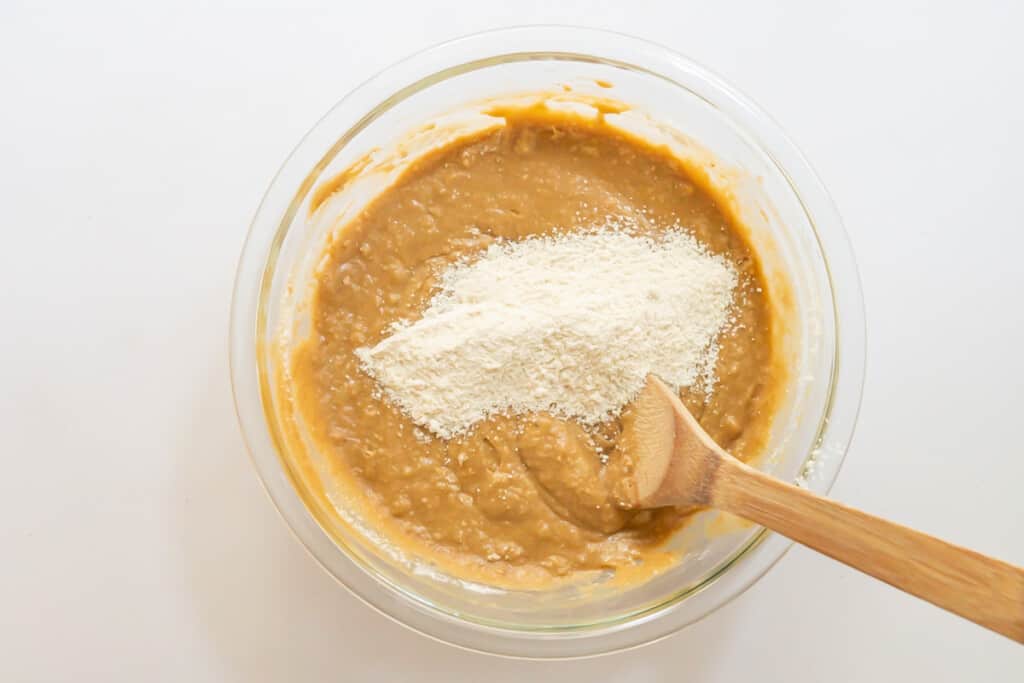 Overhead view of a bowl of cake batter with ½ cup of dry ingredient mixture ready to mix in with a wooden spoon.