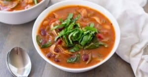 Side view of a bowl of easy instant pot minestrone soup with fresh basil to garnish.
